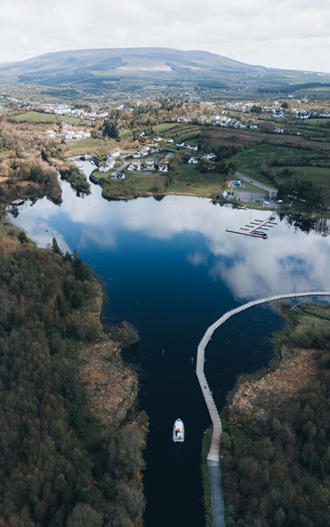 Aerial view of boat travelling up a river with a mountain in the distance.