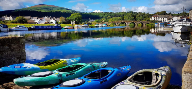 An image of Irish scenery with canoes on a river with mountain in the background