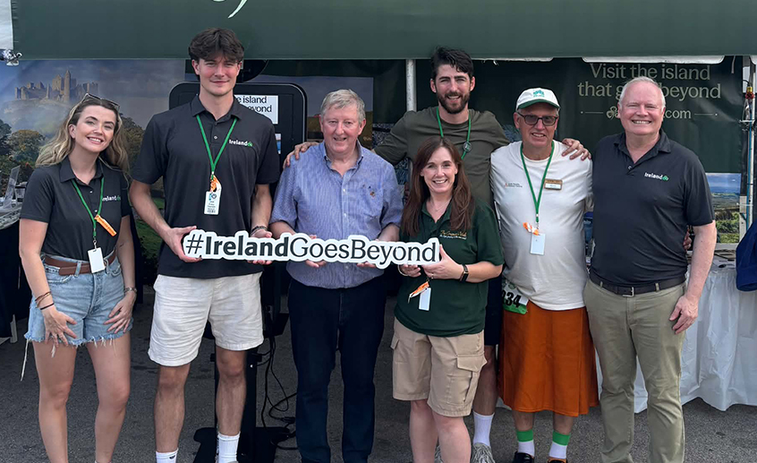 Group posing with a #IrelandGoesBeyond sign at Tourism Ireland’s stand during an outdoor event in Milwaukee.