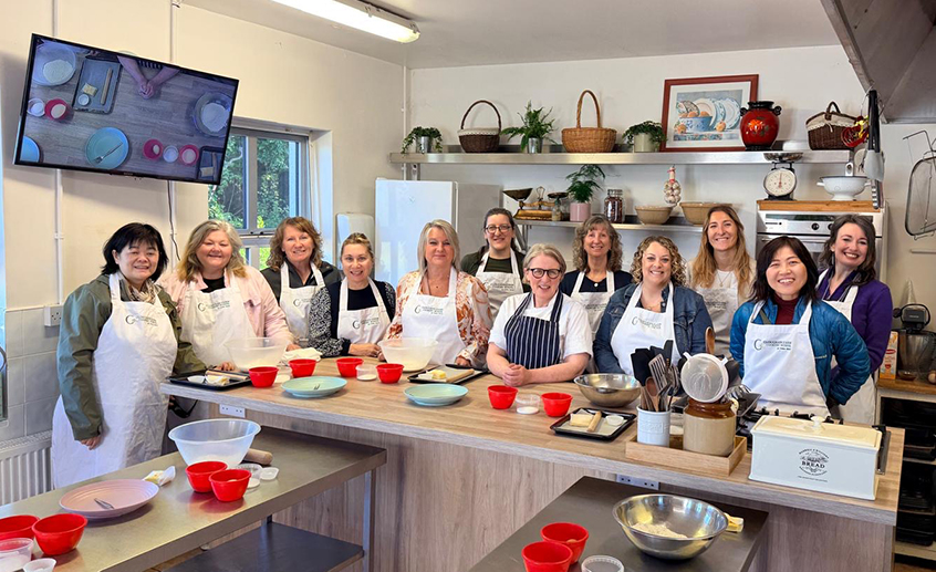 Group of participants in aprons standing around a kitchen island during a cooking class.