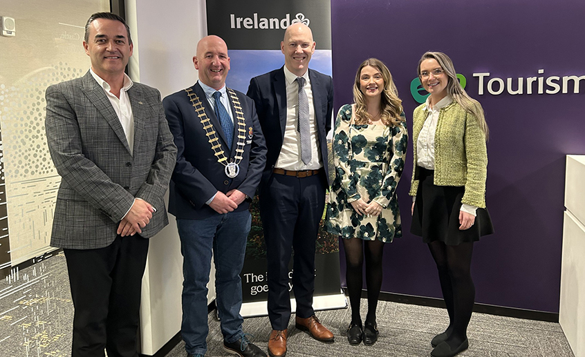 Group of five people standing indoors in front of Tourism Ireland signage.