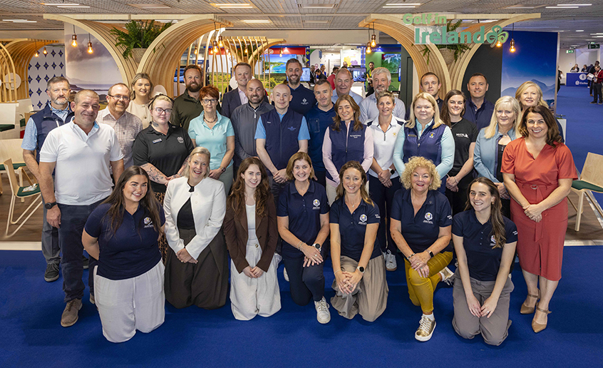 Group of people posing indoors at an event with a 'Golf in Ireland' sign in the background.