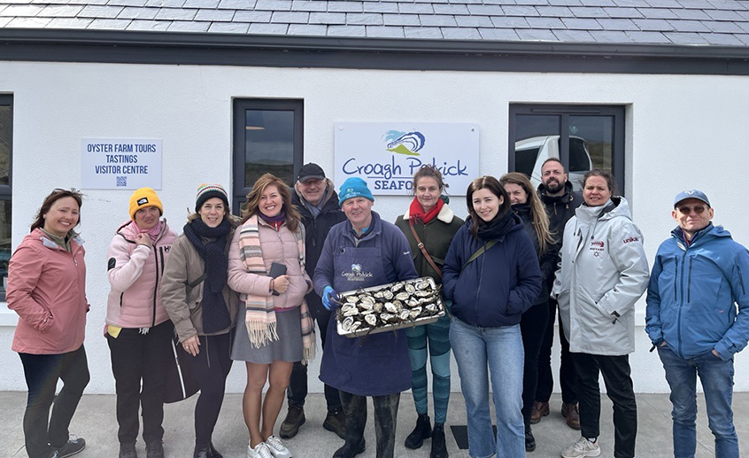 Group outside an oyster farm holding a tray of oysters.