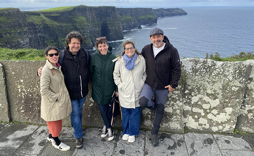 Five people standing together with dramatic cliffs and seascape in the background.