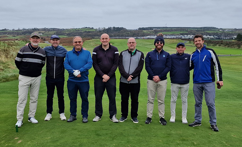 A group shot of eight people standing in a row on a golf course