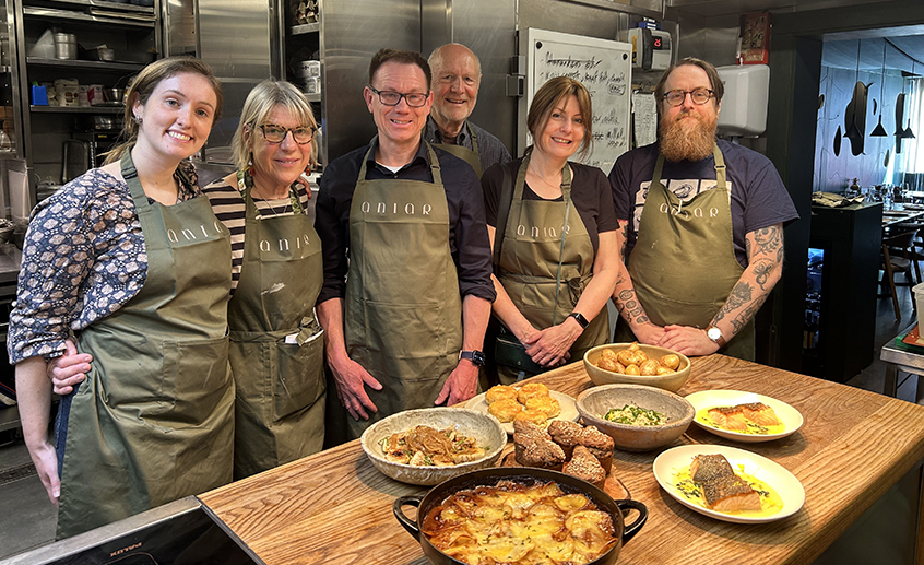 Group of chefs wearing aprons stand behind a table of prepared Irish dishes in a restaurant kitchen.