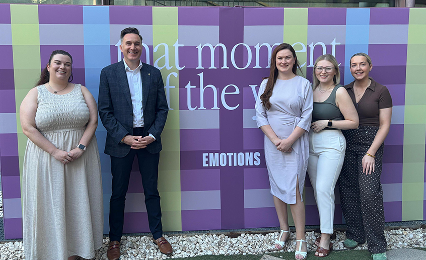 Five people standing in front of a colorful event backdrop with the word “EMOTIONS” displayed.