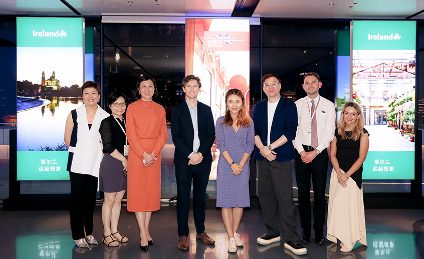 Group of people posing indoors at an Ireland promotion event with branded display panels behind them.