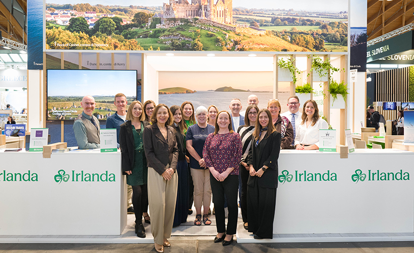Copilot said:  Tourism Ireland team at the Ireland exhibition stand during a travel trade event in Rimini, with scenic Irish landscapes displayed overhead.