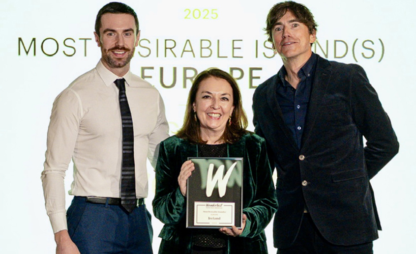 Three people standing together with the person in the center holding a plaque that reads 'Ireland', in front of a backdrop displaying the text ‘2025 Most Desirable Island(s) Europe.’