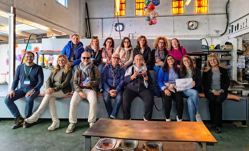 Group of people seated indoors on benches in a workshop setting.