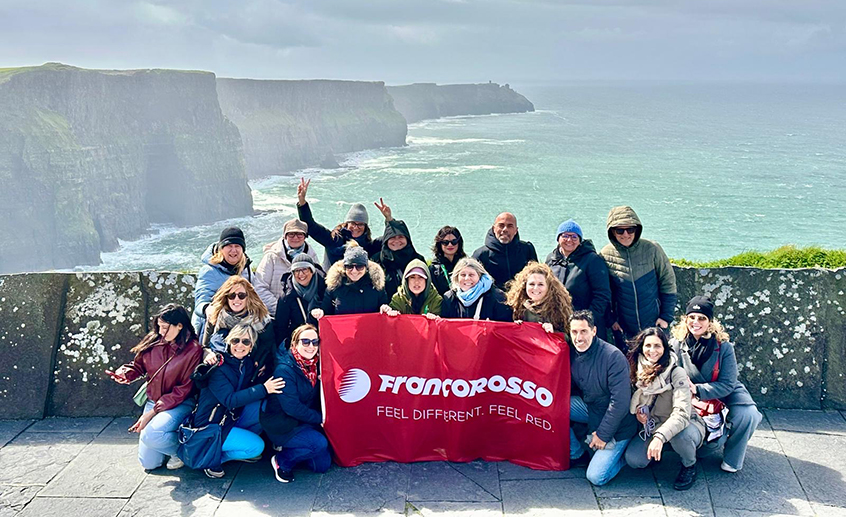 Group of travel agents holding a Franconero banner at the Cliffs of Moher overlooking the Atlantic Ocean.