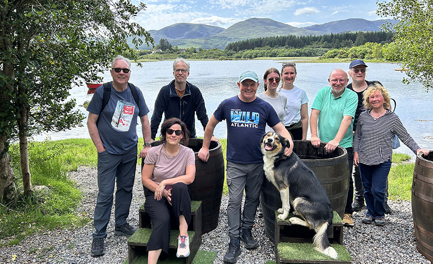 Group of people and a dog posing by a lakeside with mountains in the background.