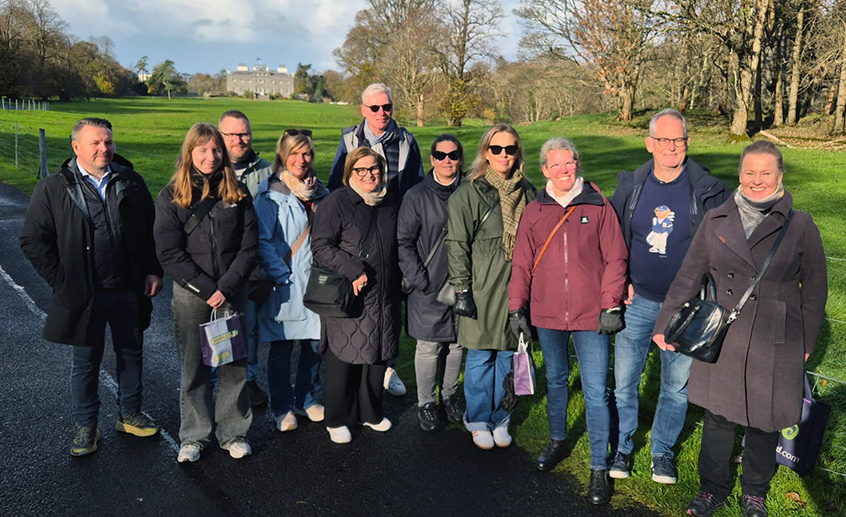 Group shot of eleven people standing on a patch of grass with a house in the distance behind them