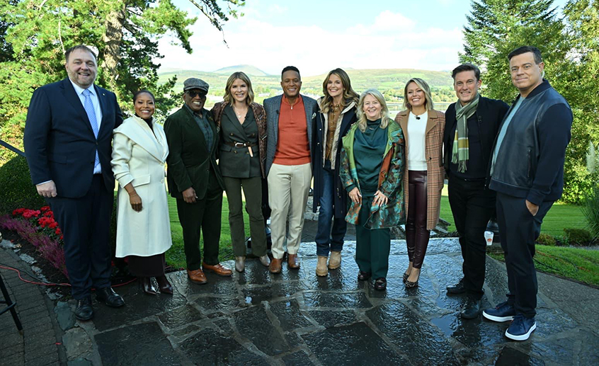 Group of visitors posing outdoors at a scenic Irish estate with lake and mountain views in the background.