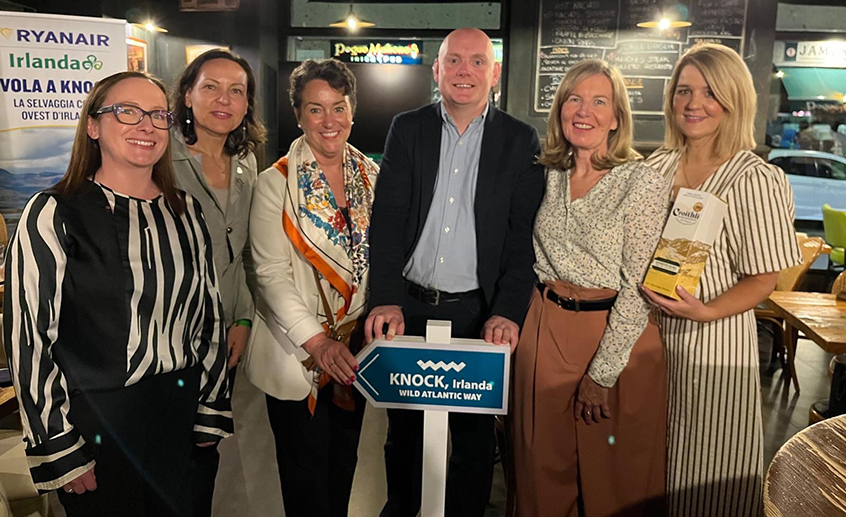Group of people indoors holding a “Knock, Ireland – Wild Atlantic Way” sign at a travel promotion event.