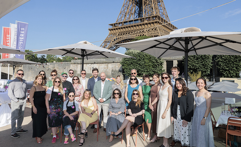 Group of people posing outdoors under umbrellas with the Eiffel Tower in the background at a tourism event.