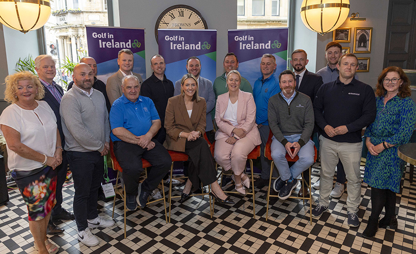 Group of people seated and standing indoors in front of “Golf in Ireland” banners.