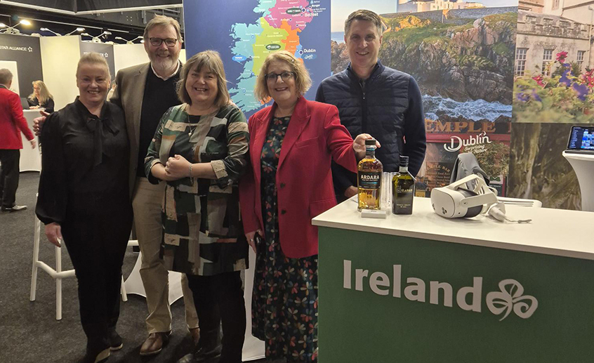 Group of five people standing at an Ireland tourism booth with a map backdrop.
