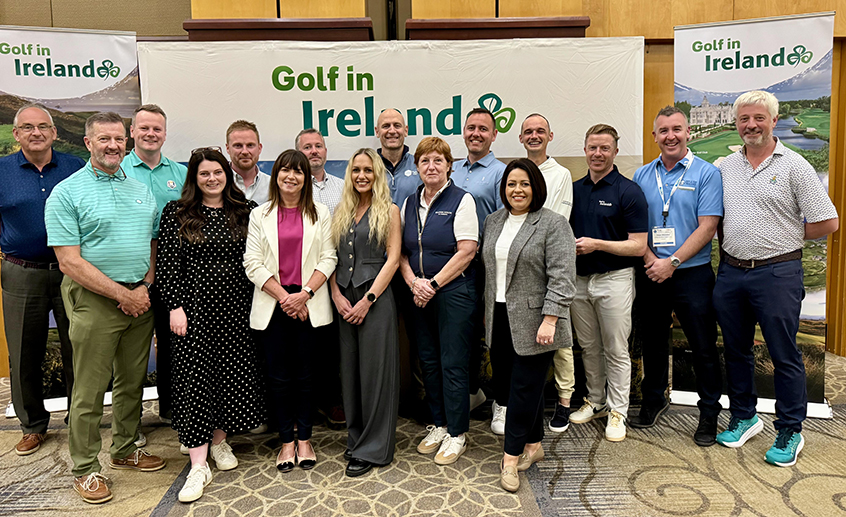 Group shot of 16 people posing at a stand with scenic imagery and the 'Golf in Ireland' logo