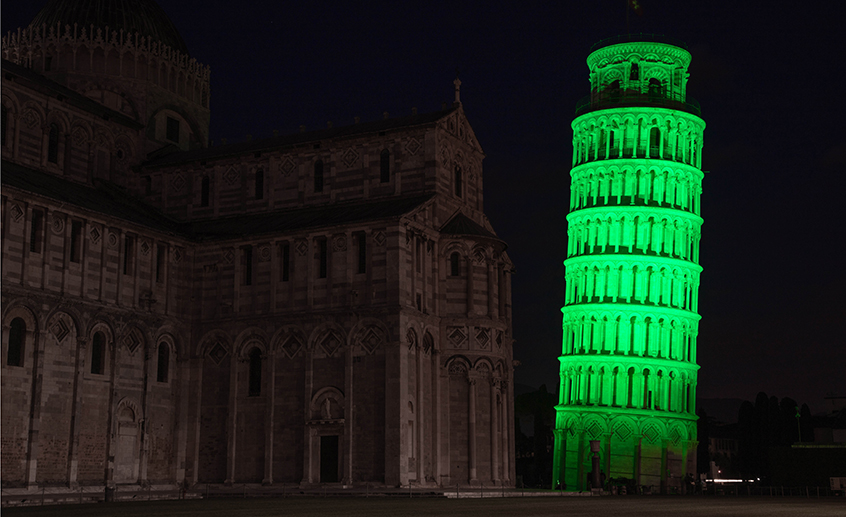 Leaning Tower of Pisa illuminated bright green beside the darkened cathedral at night.