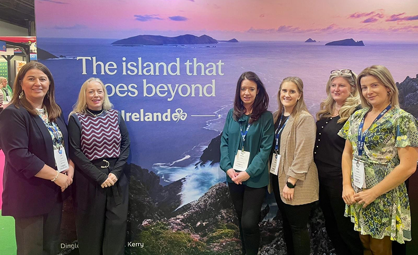 Group of people standing in front of a large promotional backdrop featuring a coastal landscape and the text “The island that goes beyond – Ireland".