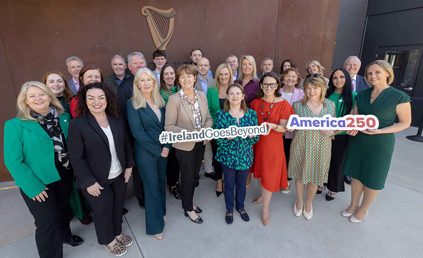 Group of adults standing outside a building, holding signs reading “#IrelandGoesBeyond” and “America250