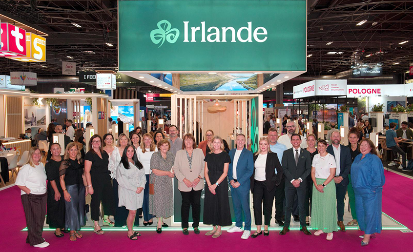 Group photo of Tourism Ireland staff and partners standing in front of the Ireland exhibition stand at a travel trade show in Paris.