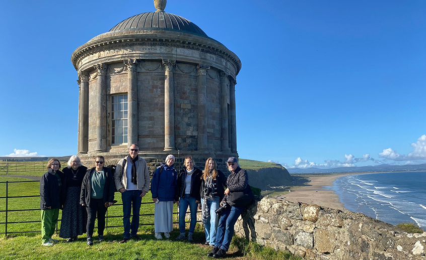 A group of people standing in front of a temple beside cliffs and sea on a sunny day.