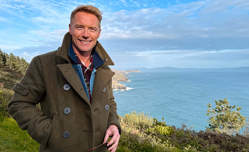 Person standing on a coastal cliff overlooking the ocean under a blue sky
