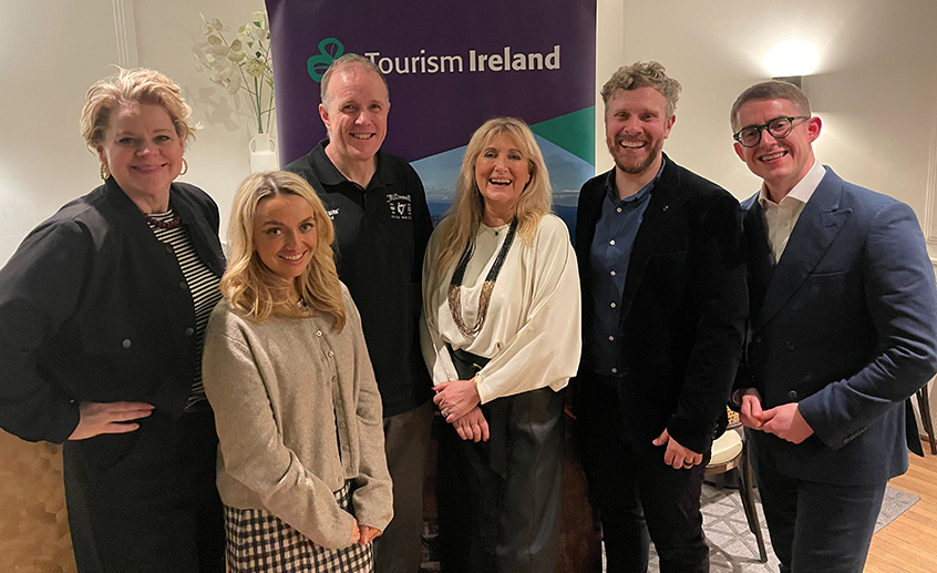 Group shot of six people standing in front of a Tourism Ireland poster