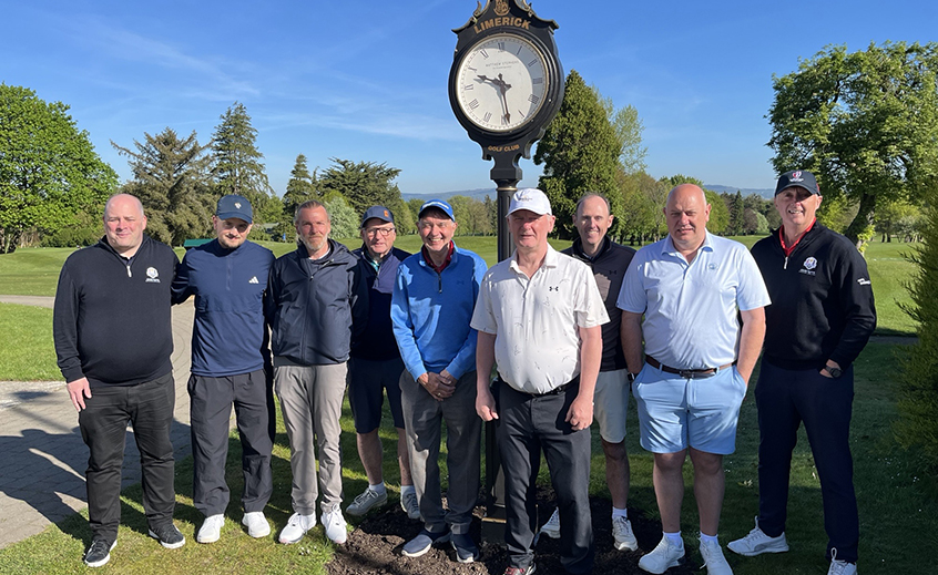 Group of golfers posing on a green beside a Limerick‑branded course clock on a sunny day.