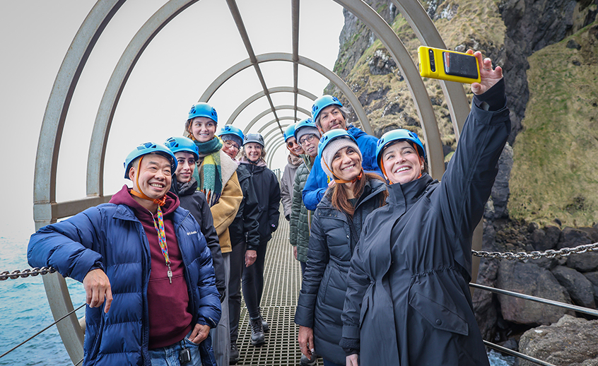 Group of people wearing helmets taking a selfie on a coastal walkway.