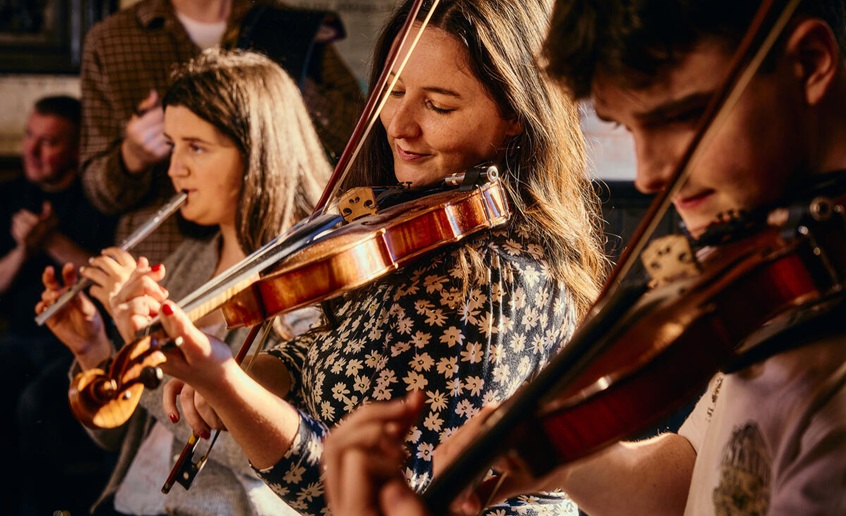 Trio of traditional music players consisting of two fiddle players and a whistle player.