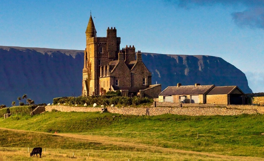 Castle with mountain in background and cow grazing on land in front.