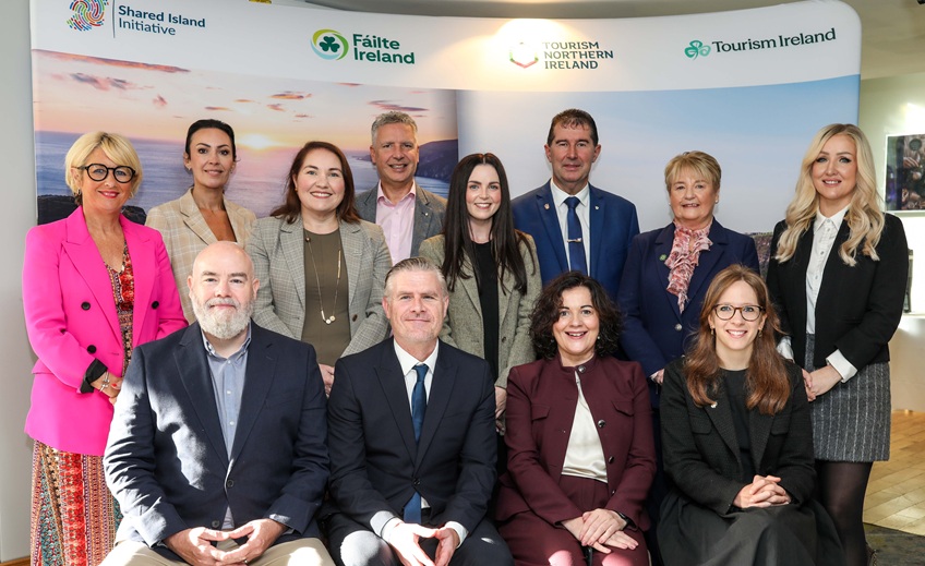 Group photo of ten people at a tourism industry event, standing and seated in front of a branded display featuring Shared Island Initiative, Fáilte Ireland, Tourism Northern Ireland and Tourism Ireland logos.