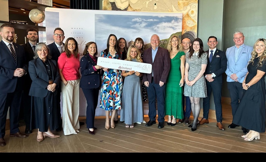 Group of people gathered at a Tourism Ireland luxury tourism event, standing in front of a branded display and holding a Tourism Ireland sign.
