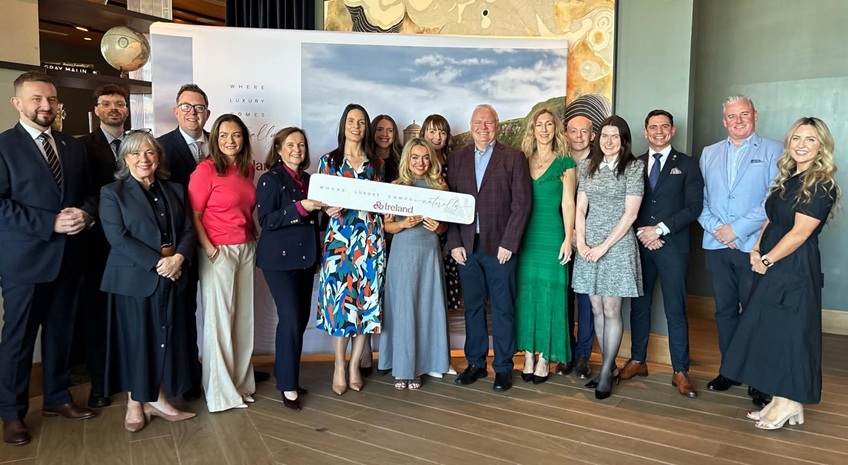 Group of people gathered at a Tourism Ireland luxury tourism event, standing in front of a branded display and holding a Tourism Ireland sign.