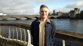Man standing in Limerick cityscape with bridge and river behind him.