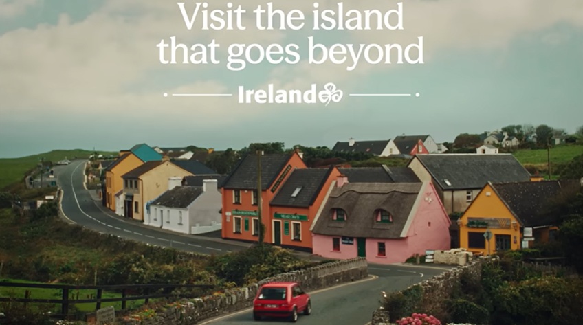 Picture of red car driving into colourful village with text saying 'Visit the island that goes beyond, Ireland'
