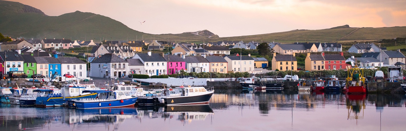 Colourful village in front of harbour with boats, mountains in background