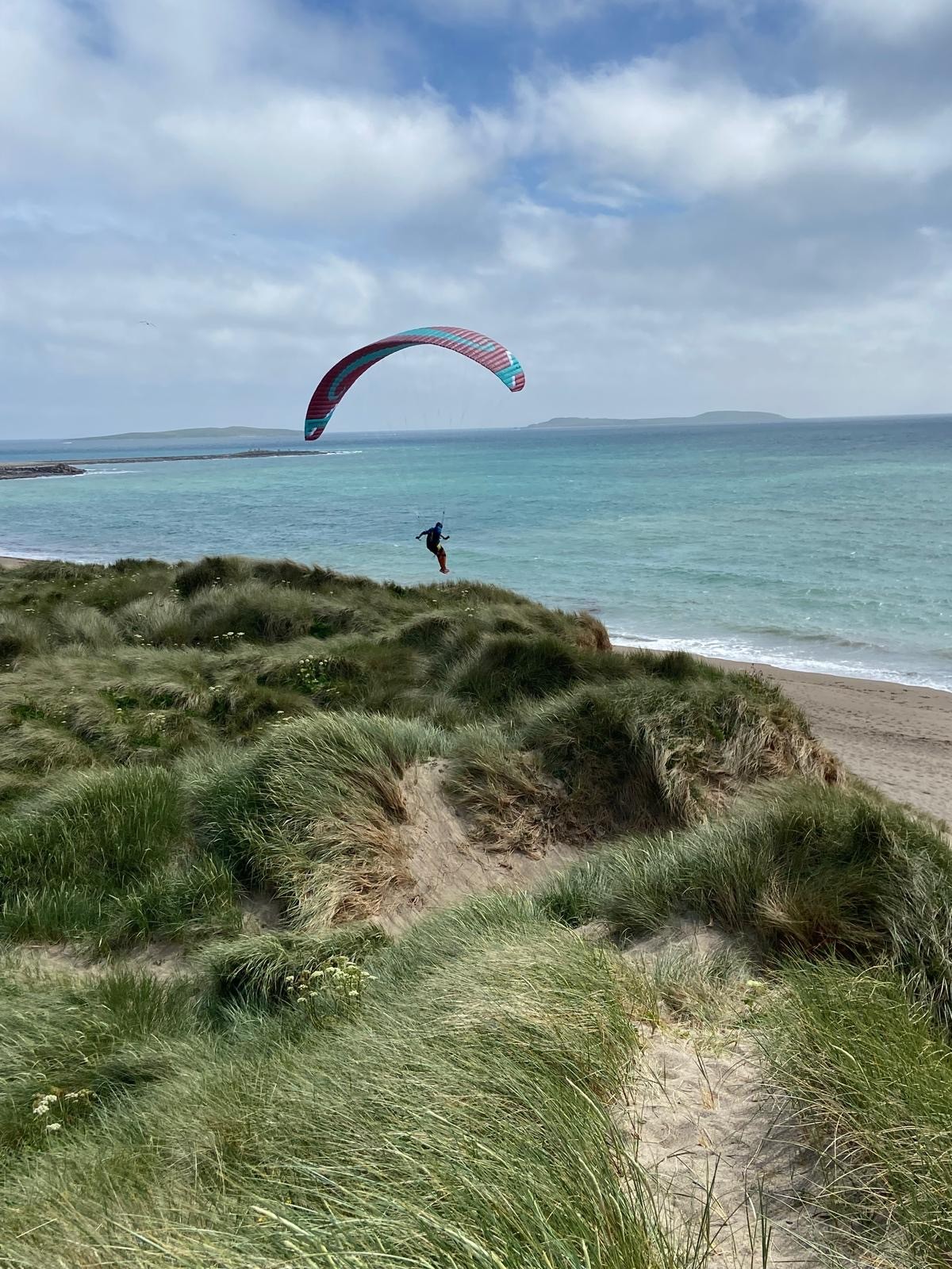 Paraglider fliegt über den Strand mit Dünen und Meer im Hintergrund