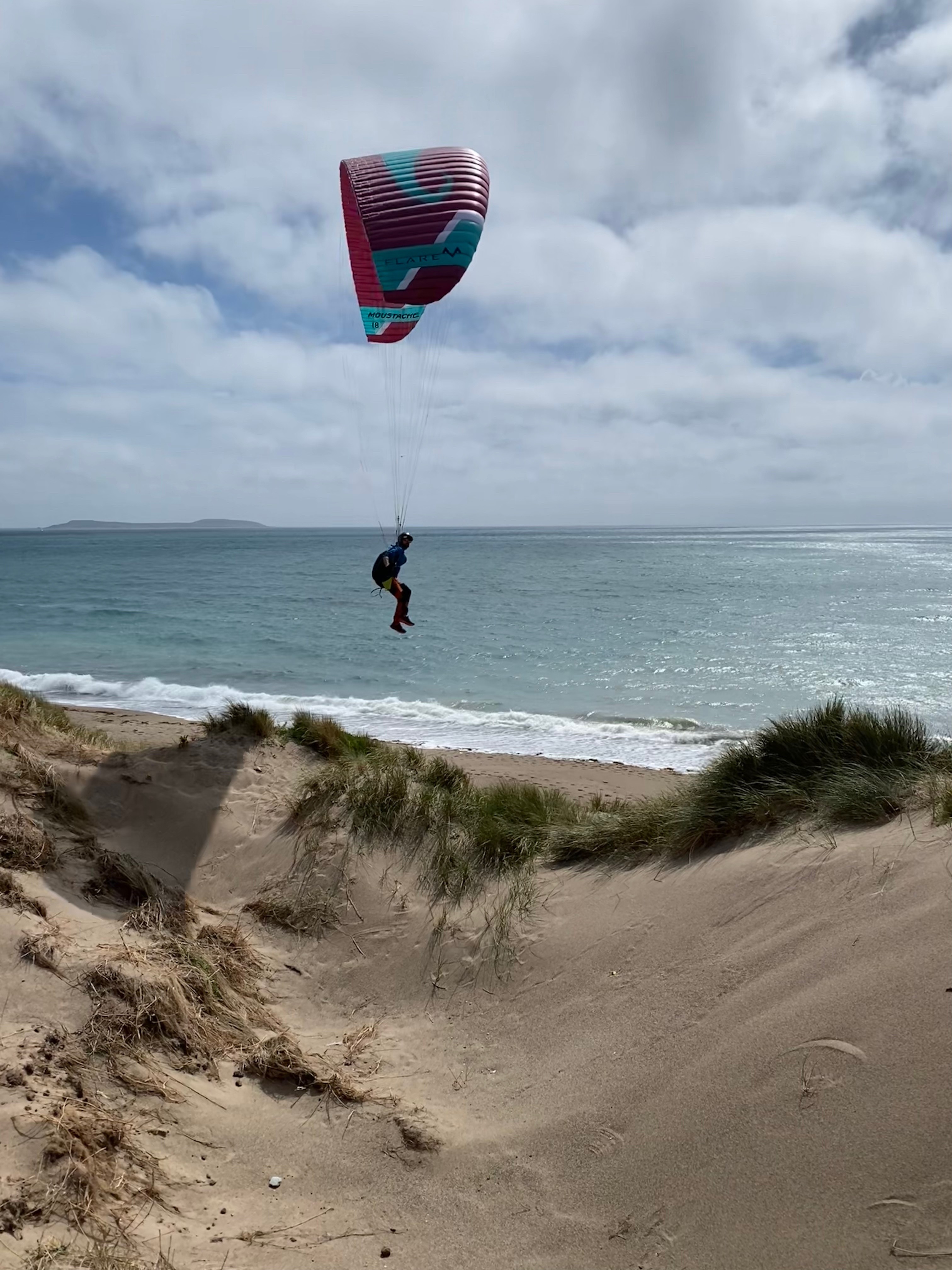Paraglider schwebt über einem Strand, dahinter sieht man Wasser